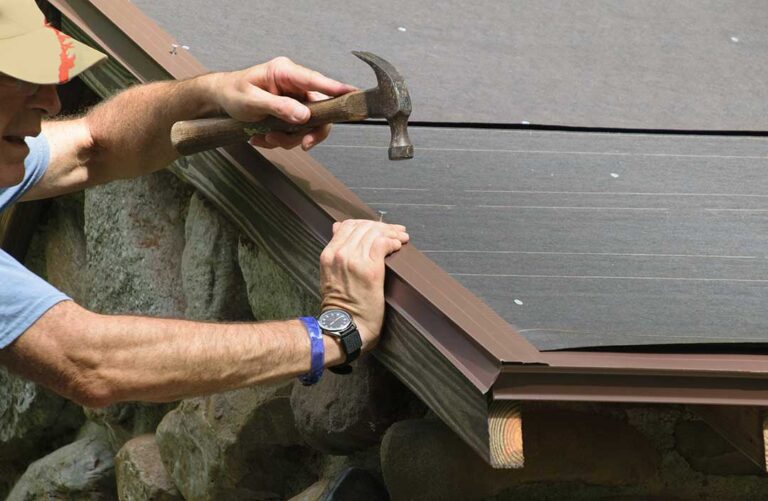 Close-up view of several hands installing new asphalt shingles on a sloped residential roof